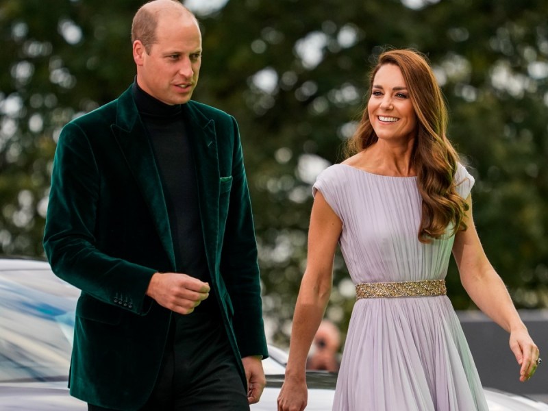 Prince William (L) in green velvet suit walking next to Kate Middleton, who is wearing a cream-colored gown