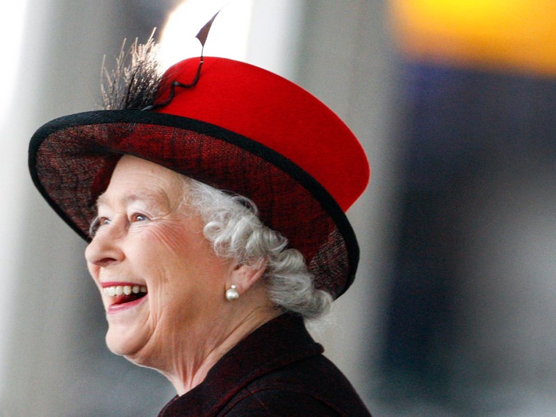 Queen Elizabeth weating a black and red hat, smiling widely