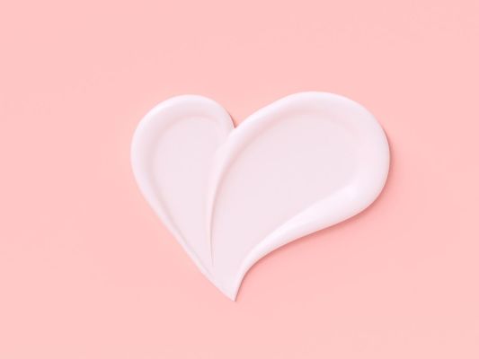 Cosmetic cream smeared in the shape of a heart on a pastel pink background