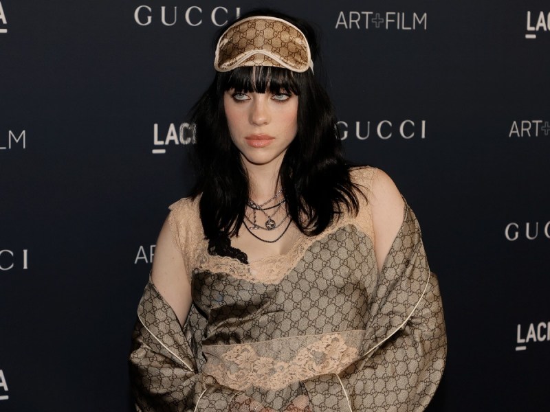Billie Eilish poses in satin outfit and sleep mask against black backdrop