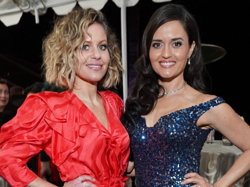 Candace Cameron Bure (L) in red dress standing next to Danica McKellar who is wearing a navy blue dress
