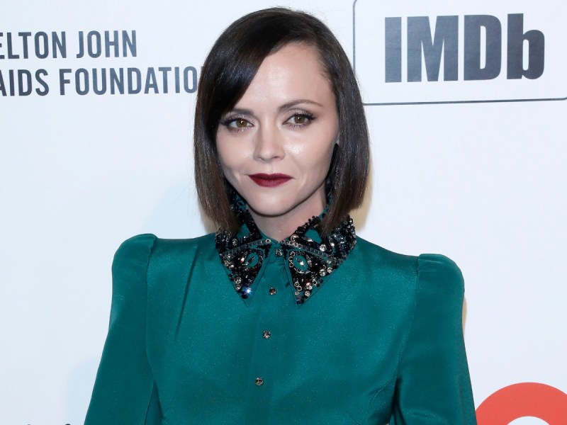 Christina Ricci smiles in teal top against white backdrop