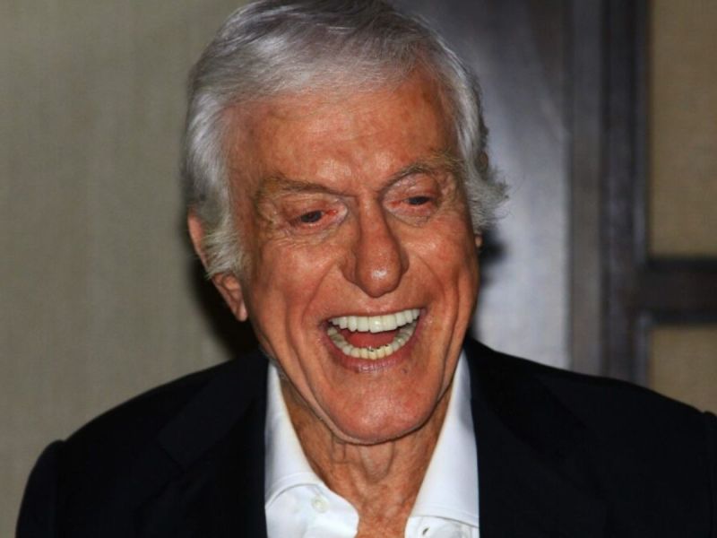 Dick Van Dyke laughing and wearing a black suit.