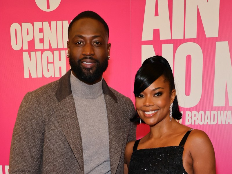 Dwyane Wade in a grey turtleneck and coat smiling with Gabrielle Union in a black dress with silver earrings