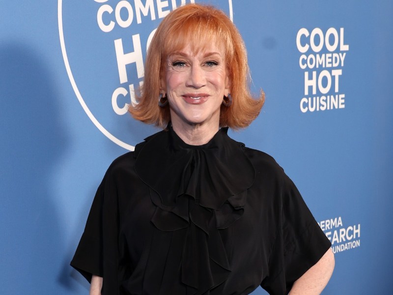 Kathy Griffin smiles in black dress against blue backdrop