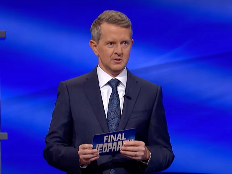 screenshot of Ken Jennings hosting Jeopardy in a navy suit and tie
