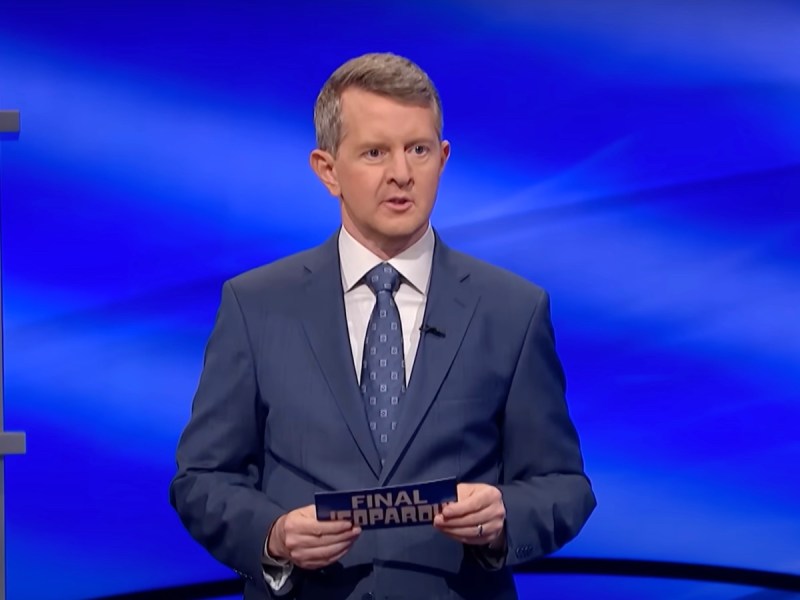 screenshot of Ken Jennings in a blue suit and tie hosting Jeopardy!