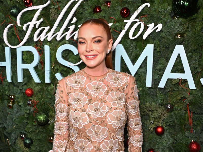 Lindsay Lohan smiling in a sheer white dress in front of Christmas decor