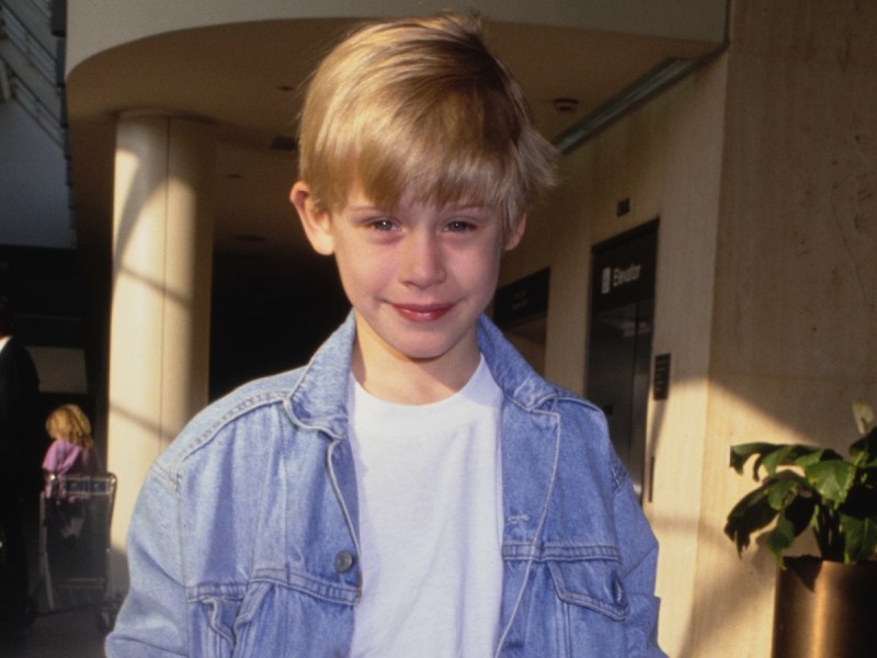 Young Macaulay Culkin smiles in white tee shirt and jean jacket