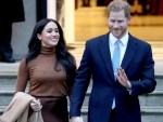 Prince Harry (R) in blue suit holding hands with Meghan Markle, who is wearing a light brown sweater
