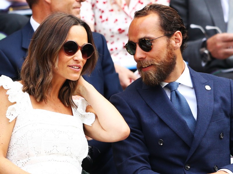 Pippa Middleton (L) in white dress and sunglasses sitting next to her husband James, who is wearing a blue suit/tie and subglasses