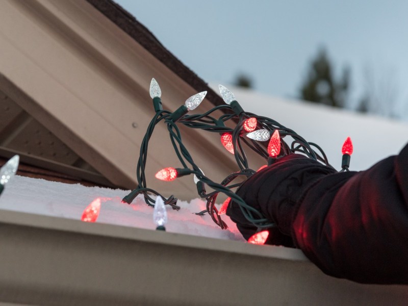 Closeup of arms hanging red and white Christmas lights on a house