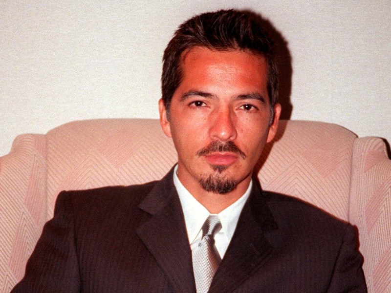 Rene Elizondo sitting in pale pink chair wearing black suit and tie