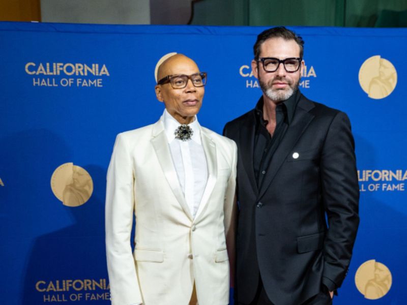RuPaul wearing a white suit and standing with his husband, Georges LeBar.
