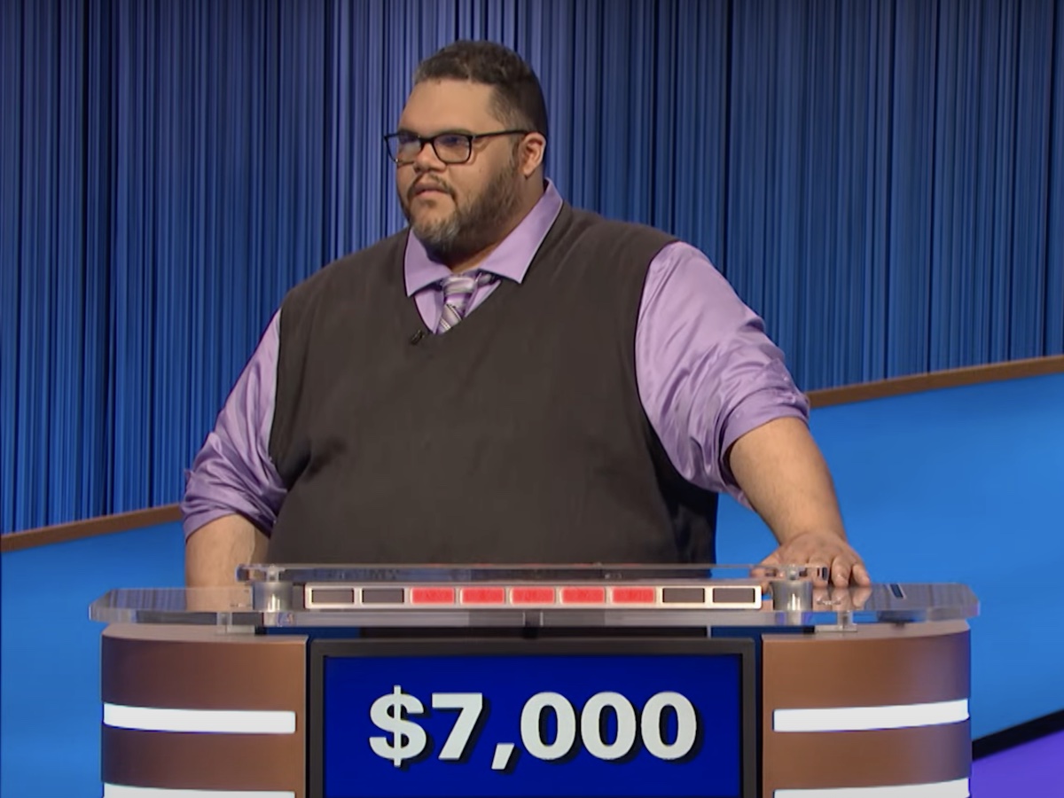 screenshot of Ryan Long competing on Jeopardy! in a purple shirt and tie and grey sweater vest