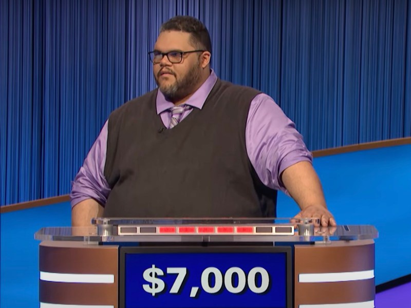 screenshot of Ryan Long competing on Jeopardy! in a purple shirt and tie and grey sweater vest