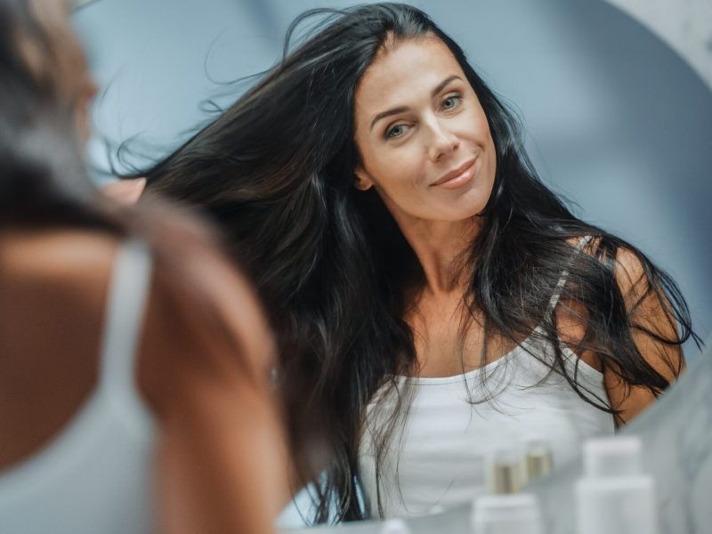 A woman touching her long, healthy hair while looking in the mirror
