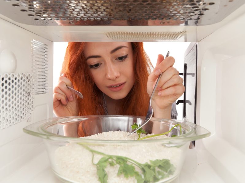 a woman checks out her rice in the microwave