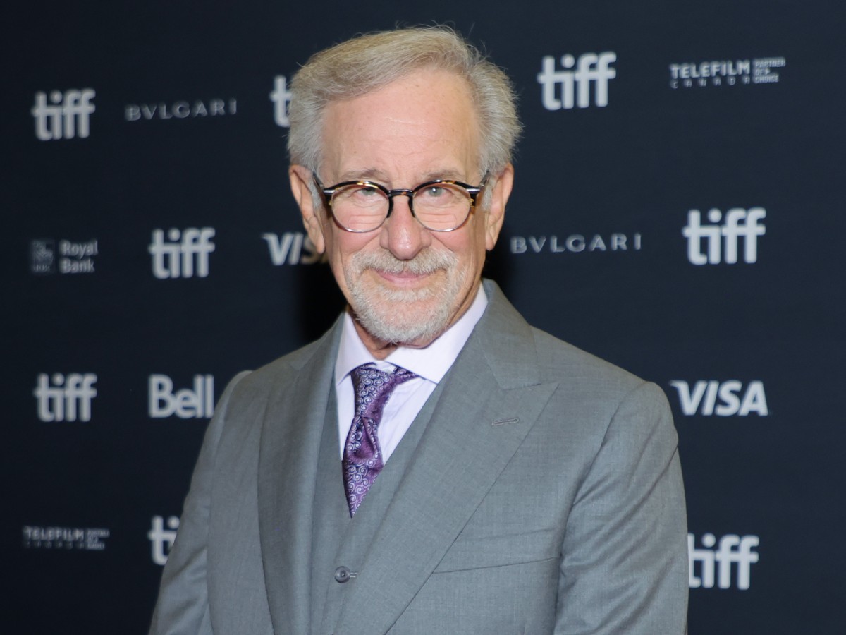 Steven Spielberg in gray suit and purple tie against back backdrop