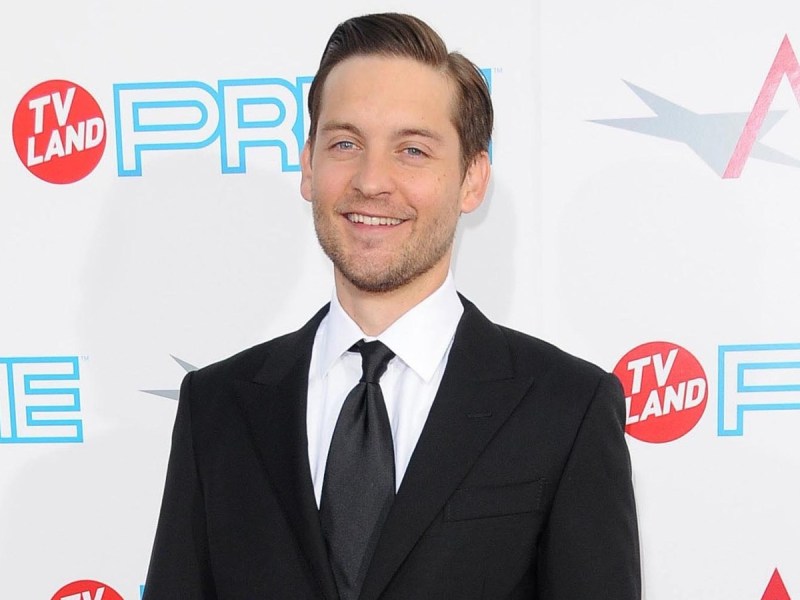 Tobey Maguire smiles in classic suit and tie against white backdrop