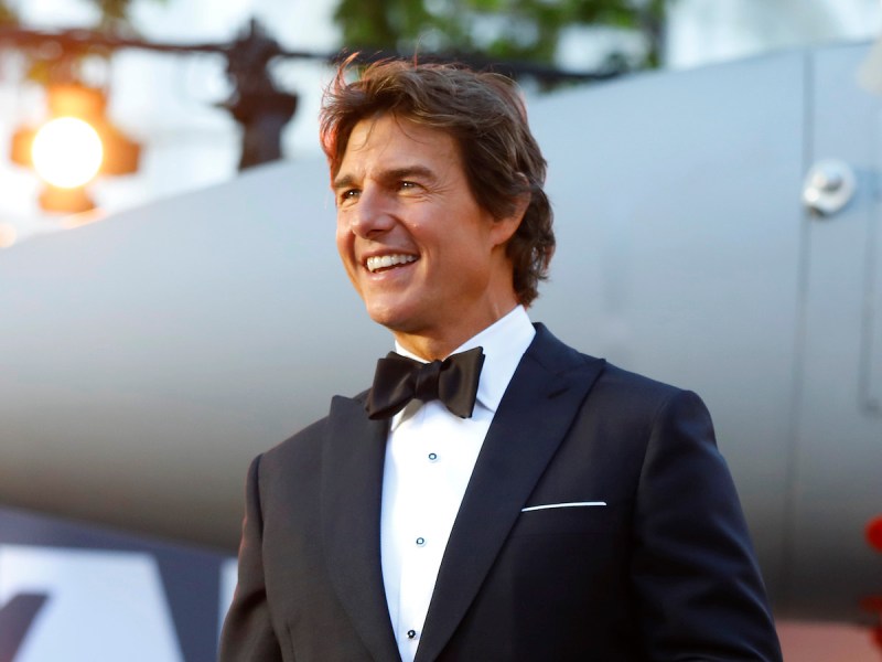Tom Cruise smiling in a tuxedo with a jet in the background