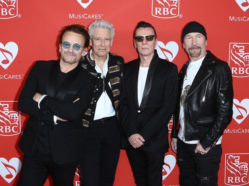 Bono, Adam Clayton, Larry Mullen Jr., and The Edge smile together all dressed in black at a charity event together