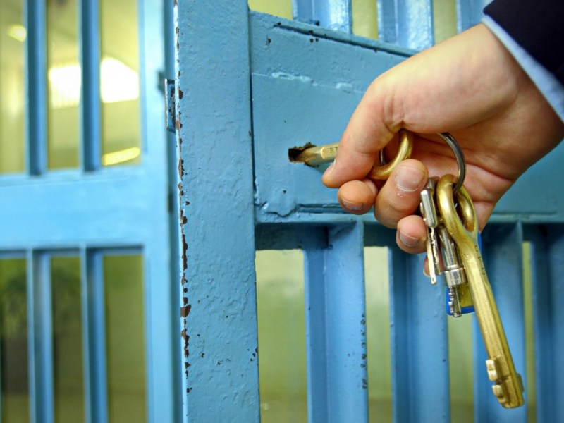 a hand holding a keyring unlocks a blue prison door