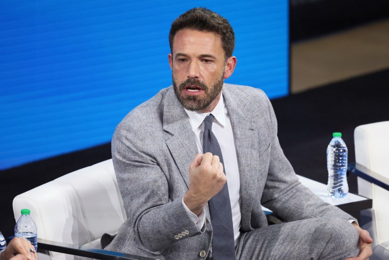 Ben Affleck sitting in a chair on stage in a grey suit pumping his fist