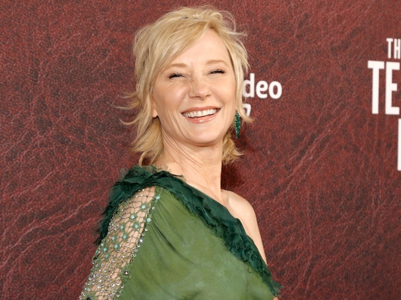 Anne Heche smiles in green dress against brown backdrop