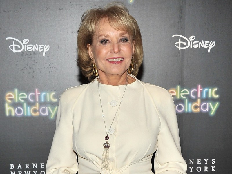 Barbara Walters smiles in off-white dress against gray backdrop