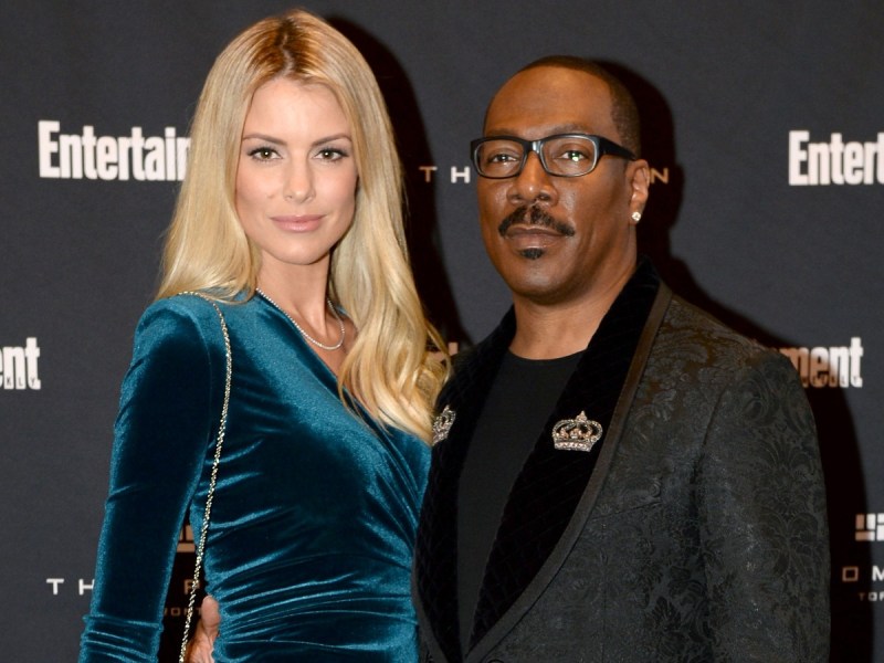 Eddie Murphy (R) in black suit standing next to Paige Butcher, who is wearing a teal velvet dress