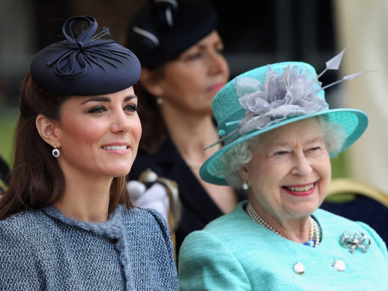 2012 photo of Kate Middleton in a blue outfit smiling sitting with Queen Elizabeth in a light blue outfit, grinning
