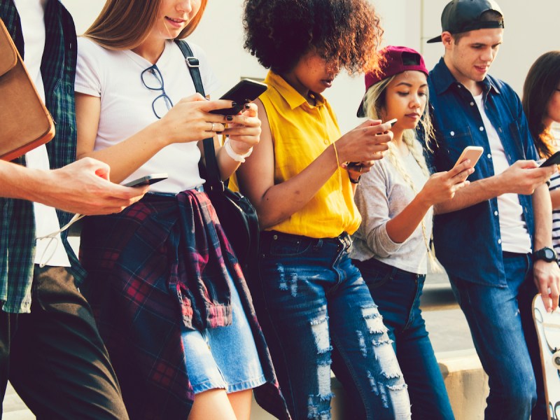 stock photo of young adults all standing in a row looking at their phones