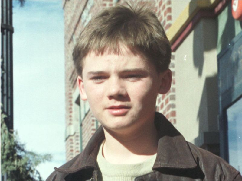 Closeup of Jake Lloyd in front of a brick building.