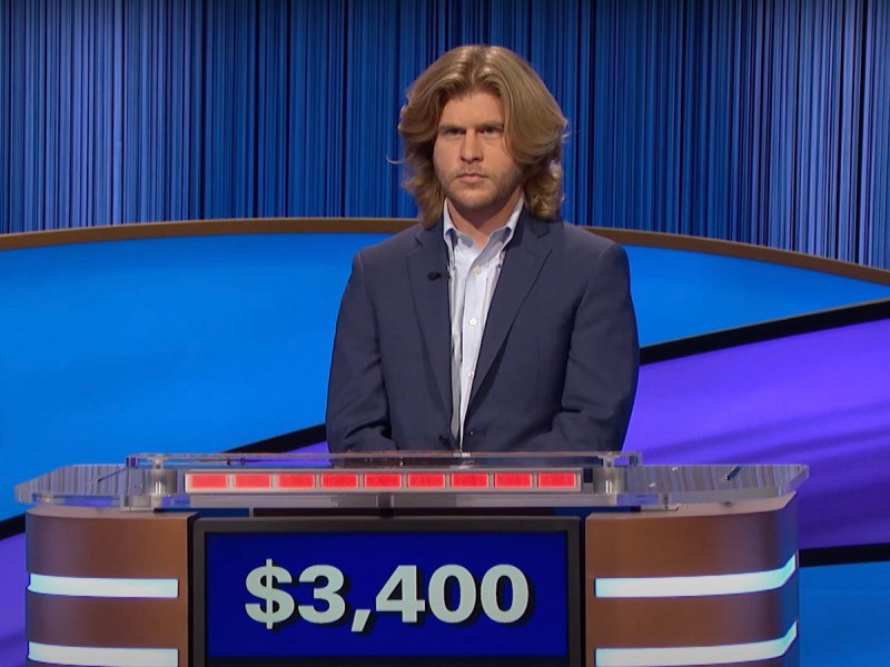 Jimmy Davoren competing on Jeopardy in a blue blazer with just above shoulder length swept blond hair that looks like what the Beegees always wanted