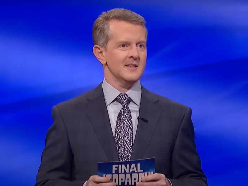 'Jeopardy!' host Ken Jennings speaks on stage holding cue card