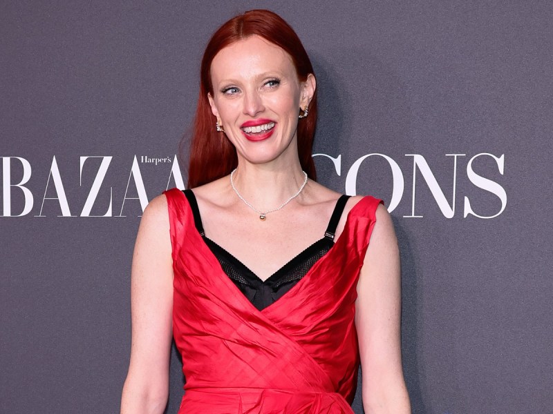 Karen Elson smiles in red dress with black undergarment peeking out