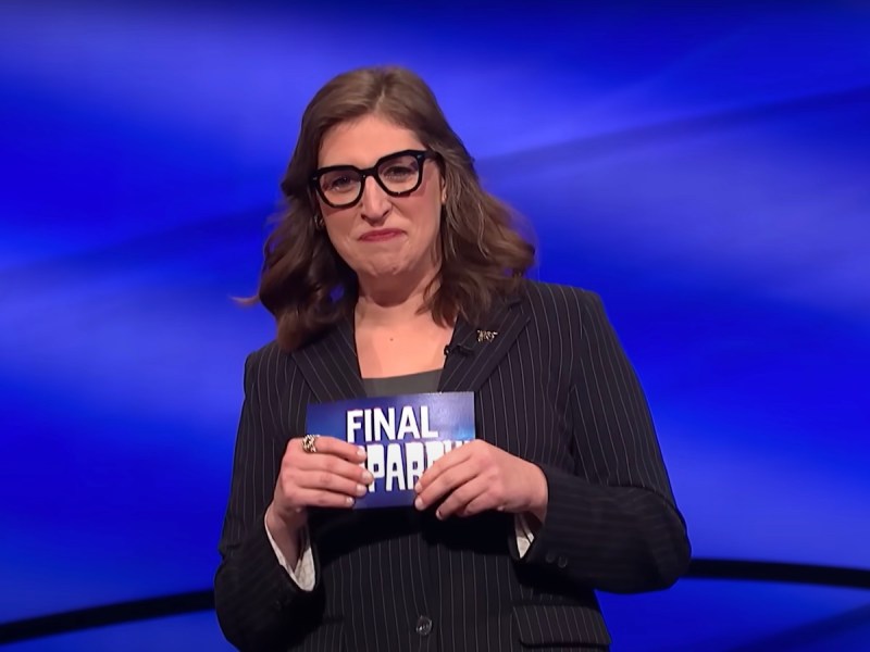 screenshot of Mayim Bialik in a black suit hosting Jeopardy