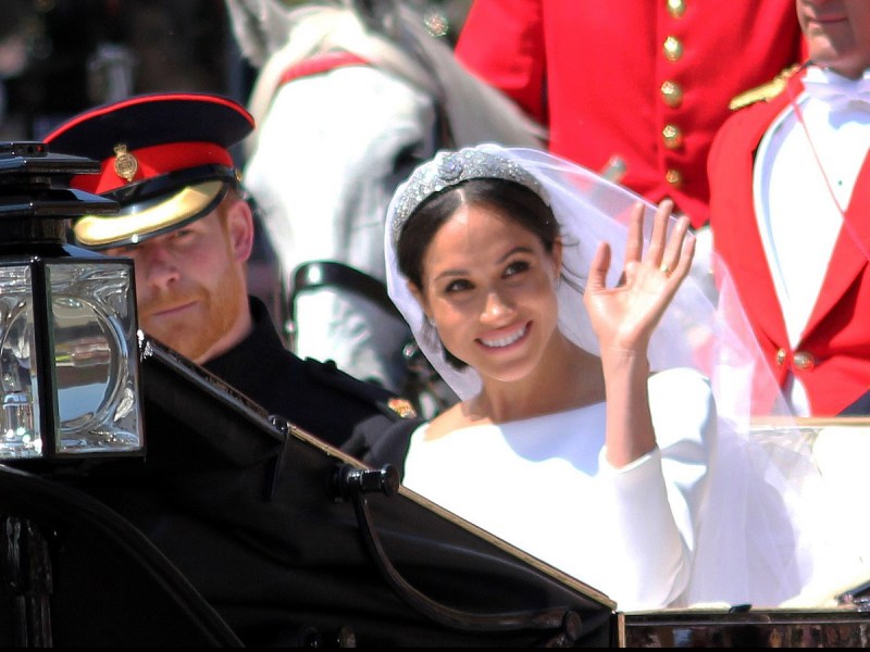 closeup of Meghan Markle and Prince Harry riding in a carriage on their wedding day with Meghan waving wearing her wedding dress and silver tiara