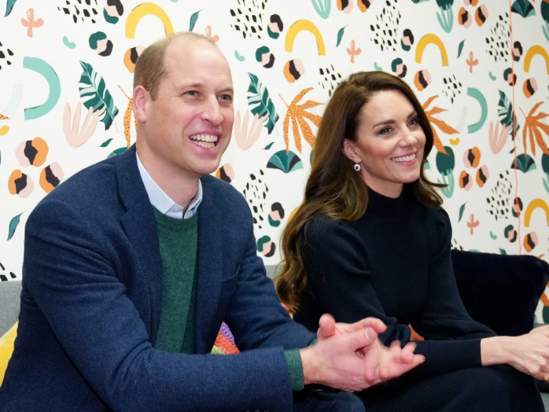 Prince William (L) and Kate Middleton smiling against patterned backdrop