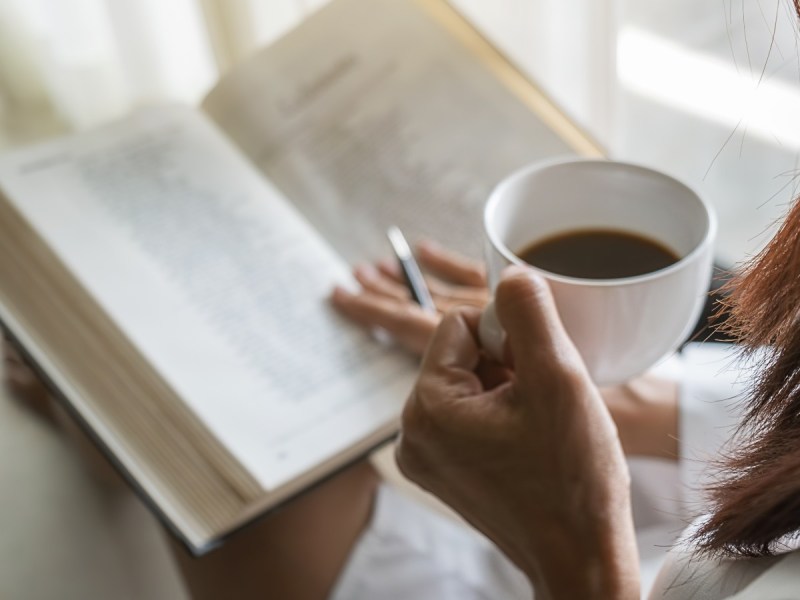 Stock photo of hand holding book and other hand holding mug of coffee
