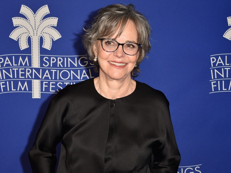 Sally Field smiles in black shirt against royal blue backdrop