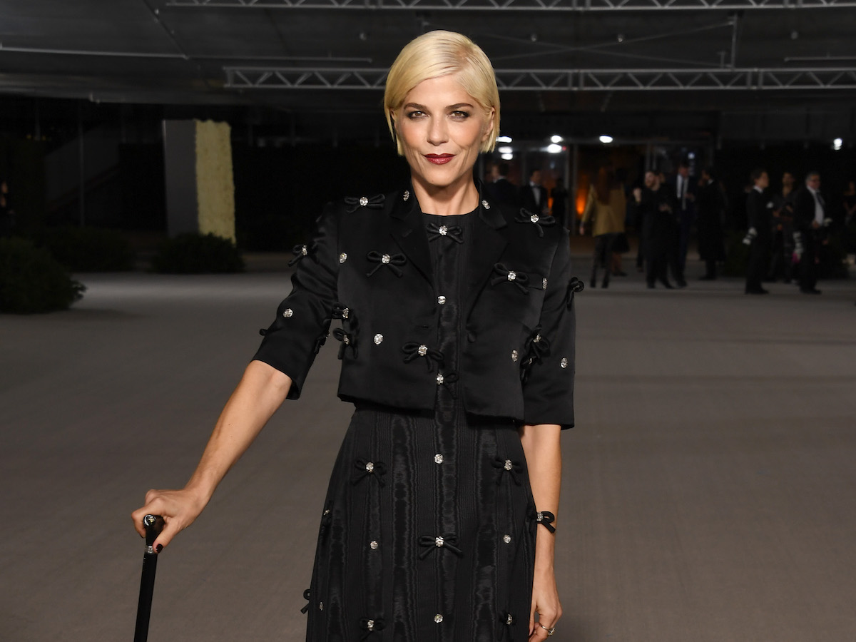 Selma Blair posing in a black dress holding a cane with a sly smile