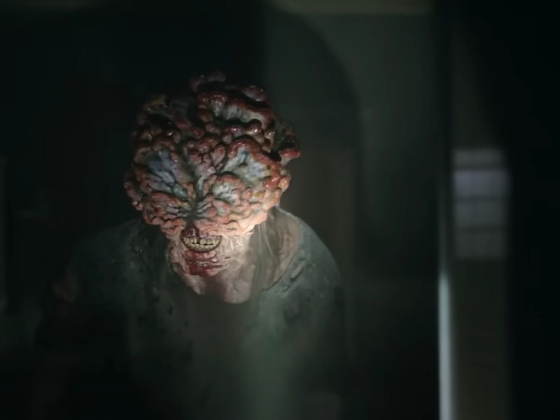 screenshot of a clicker, a human body with fungus overtaking its head, lit by a flashlight in a dim room