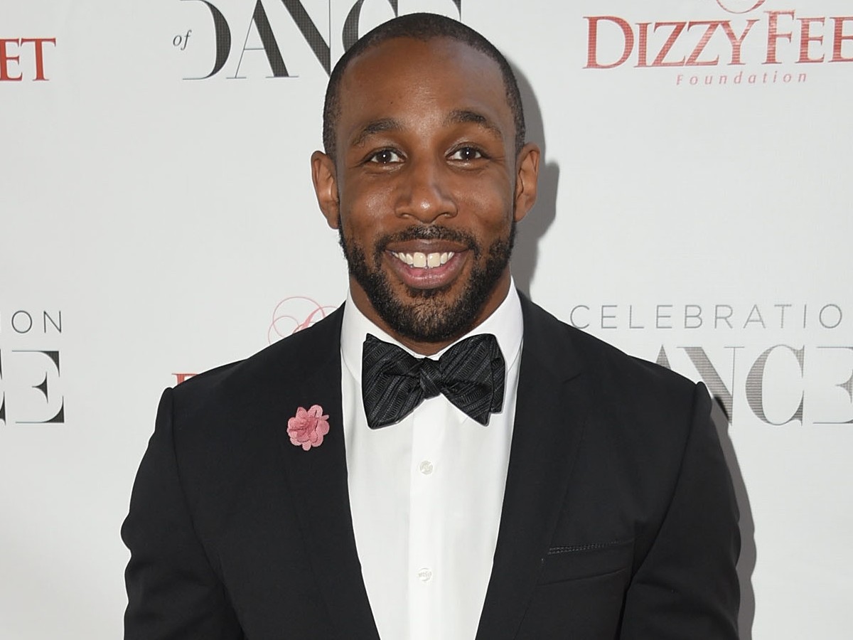 Stephen 'tWitch' Boss smiles in classic black suit and bowtie against white backdrop
