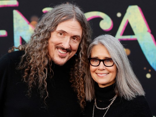 Weird Al (L) and his wife Suzanne smile together, both wearing black outfits