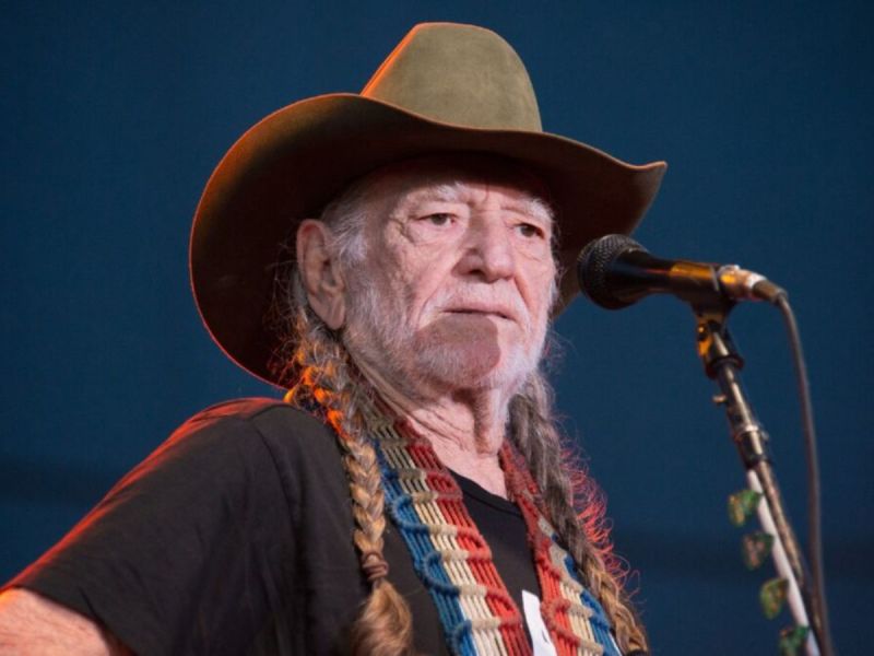 Willie Nelson wearing a black shirt and a green cowboy hat while performing on stage.