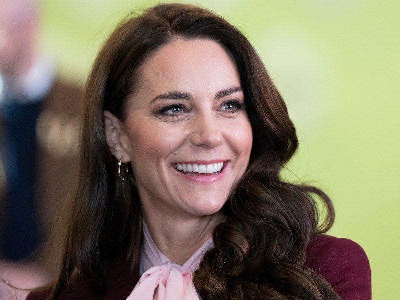 Kate Middleton smiles in closeup image while wearing pale pink scarf and burgundy jacket