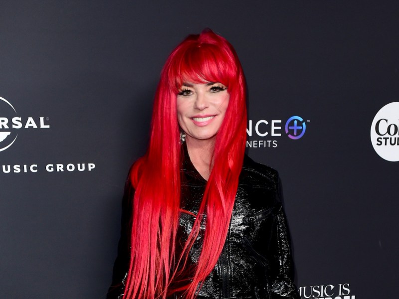 Shania Twain smiling in a black leather top with long bright red hair