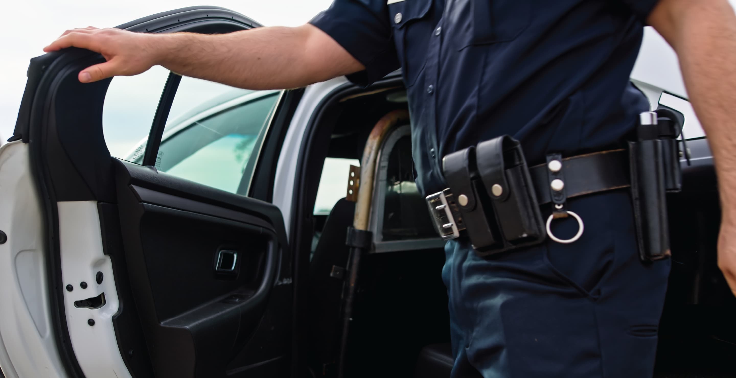 Police Officer Holding Passenger Door Of Squad Car